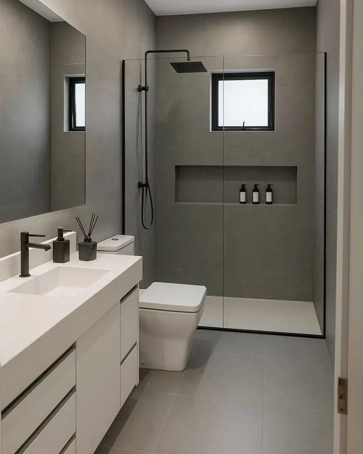 Baño minimalista terminado, con ducha a ras de piso, mampara de vidrio, nicho embutido y porcelanato gris